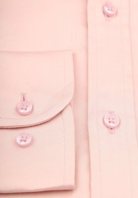 Lichtroze shirt met een borstzakje, knopen en nette stikdetails. De stof lijkt glad met een subtiele glans.