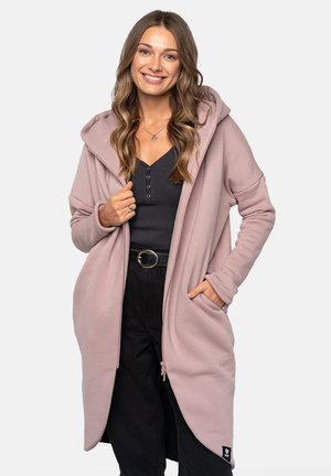 Długi różowy hoodie wykonany z miękkiego materiału, z przednim zamkiem błyskawicznym, dużym kapturem i bocznymi kieszeniami. Ma luźny krój i ściągacze na rękawach.