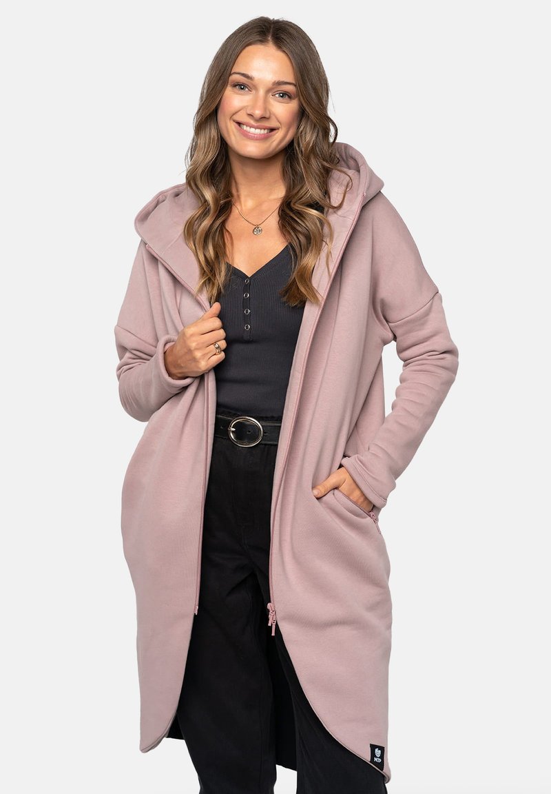 Długi różowy hoodie wykonany z miękkiego materiału, z przednim zamkiem błyskawicznym, dużym kapturem i bocznymi kieszeniami. Ma luźny krój i ściągacze na rękawach.