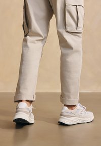 Světlé šedé tenisky vyrobené z mesh a semišového materiálu, s reflexními akcenty a bílým podpatkem. Nosí se s světlými béžovými cargo kalhotami s manžetami.