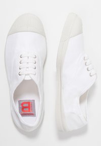 Sneakers bianchi in tela con punta e suola in gomma testurizzata, caratterizzati da sei occhielli e una fodera in tessuto. Etichetta del marchio in rosso e grigio.