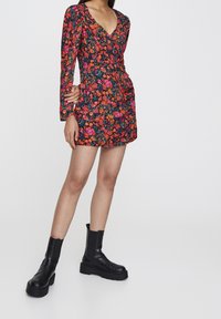 Vestido negro de flores con mangas largas, que presenta vibrantes flores rojas y naranjas. Combinado con botas negras de tobillo grueso.