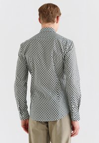 Koszula z długim rękawem, wykonana z białej tkaniny z czarnym wzorem w romby, o dopasowanym kroju i klasycznym kołnierzyku, widoczne szycie na rękawach.