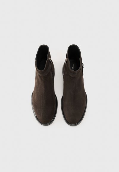 Bottines en suede marron avec une finition lisse, détail de zip sur le côté et une semelle noire en caoutchouc subtile. Design minimaliste et silhouette élancée.