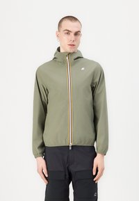 Chaqueta ligera de color verde oliva con cierre de cremallera, capucha y una raya multicolor a lo largo de la cremallera. Cuenta con puños elásticos y un logo.