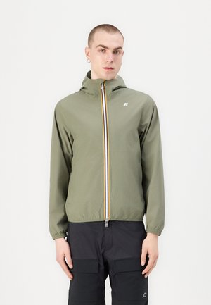Chaqueta ligera de color verde oliva con cierre de cremallera, capucha y una raya multicolor a lo largo de la cremallera. Cuenta con puños elásticos y un logo.