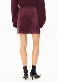 Burgunderfarbenes Samt-Minirock mit glatter Textur, einfachem Design, Seitennähten und kombiniert mit schwarzen Ankle Boots.