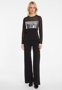 Zwart langemouwen top met een met pailletjes bedekte rechthoekige sectie, gecombineerd met brede zwarte broek met subtiele sprankelingen.