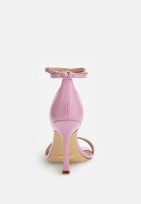 Sandalo con tacco alto in vernice rosa, dotato di un sottile cinturino alla caviglia e punta aperta. Presenta un tacco stiletto slim e una soletta tramata.