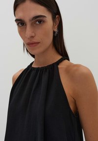 Top senza maniche nero con scollatura arricciata, realizzato in tessuto leggero. Texture liscia, cade elegantemente con un design della schiena scoperta.