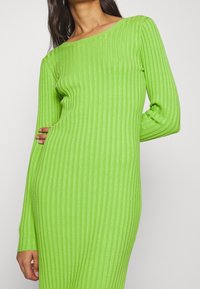 Abito lungo verde a coste con scollatura leggermente off-shoulder e silhouette aderente. Tessuto morbido con una finitura testurizzata.