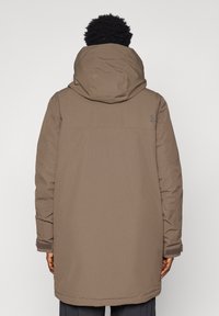 Brun, knælang dunjakke med en stor hætte, elastiske ærmekanter og en diskret logodetalje på den øverste del af ryggen. Glat ydre tekstur.