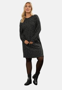 Abito lungo a maniche lunghe con stampa leopardata verde scuro, dalla vestibilità rilassata, scollo rotondo e texture morbida. Abbinato a stivaletti neri alla caviglia.