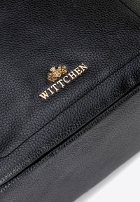 Sac à main en cuir noir avec une surface texturée. Présente le logo doré "WITTCHEN" et un détail de logo complexe. Design droit et structuré.