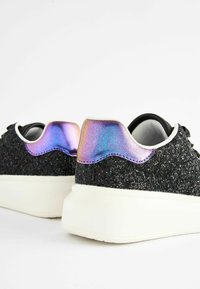 Schwarze Glitzerturnschuhe mit weißen Sohlen; verfügen über einen schimmernden Fersenakzent und glatte schwarze Schnürsenkel, die ein strukturiertes Oberdesign präsentieren.