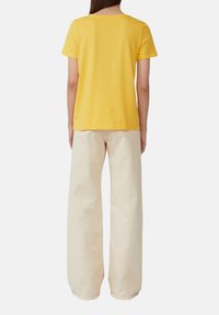 T-shirt jaune à manches courtes avec un col rond, associé à un pantalon large en beige clair à coupe ample. Tissu doux, design décontracté.