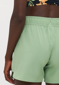 Grønne treningsshorts med elastisk midje, med en glatt tekstur og sidelufter for enkel bevegelse og ventilasjon.