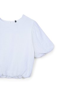 Blouse blanche texturée avec des manches courtes bouffantes, un col rond et un ourlet élastiqué. Le tissu semble léger et légèrement froissé.