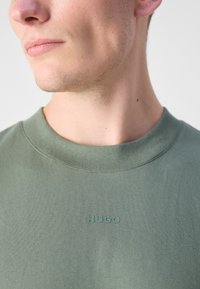 T-shirt en coton vert avec un col rond et un logo "HUGO" embossé sur la poitrine. Texture lisse et design ajusté.