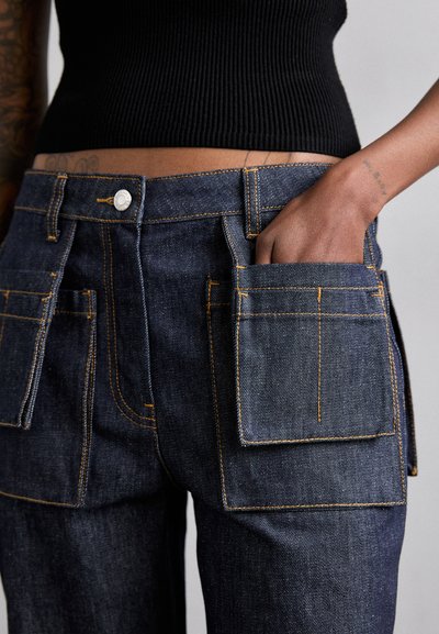 Pantaloni din denim de culoare albastru închis, cu buzunare mari în față. Cusuturi contrastante în nuanțe de portocaliu și închidere cu un nasture metalic. Textură netedă și design structurat.