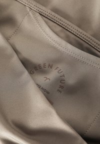 Tessuto beige con una texture liscia presenta un logo con la scritta "IL FUTURO VERDE" e "COMINCIA ADESSO" in caratteri marroni a rilievo.