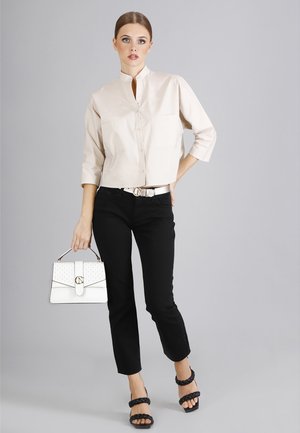 Camicia beige corta con colletto stand, jeans neri, tacchi intrecciati neri e una borsa bianca con accento dorato e dettaglio a pois.