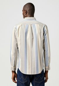 Camisa de manga larga con rayas verticales en azul claro, beige y topo. Puños con botones y un pliegue trasero para mayor comodidad.