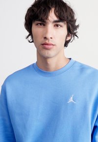 Kék pamut crewneck pulóver, bal melleden egy kis fehér hímzett logóval. Simára kidolgozott anyag, laza fazonnal.