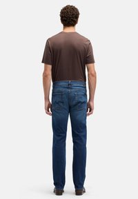 Brązowy męski t-shirt i niebieskie dżinsy z prostą nogawką, z tylnymi kieszeniami i prostym wzorem. Materiał wydaje się miękki, styl casual.