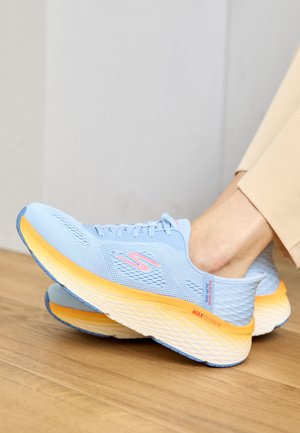 Zapatillas de running azules con parte superior de malla, acentos en rosa y naranja, y suela gruesa distintiva etiquetada como "MAX CUSHION". Fondo de suelo de madera.