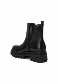 Botas de tobillo de cuero negro con cremallera lateral, suela gruesa y acabado suave. Diseño corto y ceñido con una correa en la parte trasera.