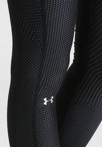Czarne legginsy sportowe z teksturowanym wzorem w trójkąty, wykonane z elastycznego materiału, z małym białym logo na dolnej części nogi.