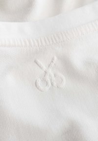 Witte stof met een ribbelstructuur toont subtiel geborduurde scharen in het midden. Het ontwerp is minimaal en monochromatisch.