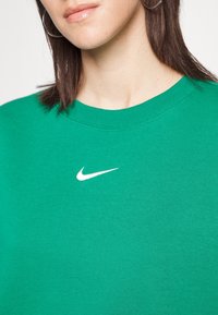 Sweatshirt vert en mélange de coton, avec un col rond et un petit logo Nike blanc sur la poitrine. Texture lisse.