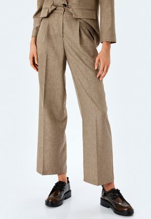 Pantalones de vestir en marrón claro, con un tejido texturizado, corte de pierna ancha y pliegues en la parte delantera, combinados con zapatos negros de cordones.