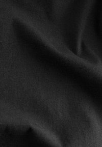 Tissu noir avec un tissage texturé subtil et des plis doux créant des ombres et des reflets délicats.