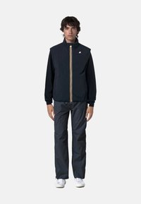 Gilet blu con colletto alto e zip, presenta righe verticali a contrasto. Abbinato a pantaloni grigi dalla vestibilità ampia e sneakers bianche.