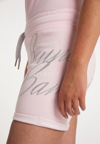 Rosa Baumwollshorts mit einer Kordelzugtaille, verziert mit silbernem Glitzertext und umgeschlagenen Säumen. Weiche Textur mit einem lässigen Design.