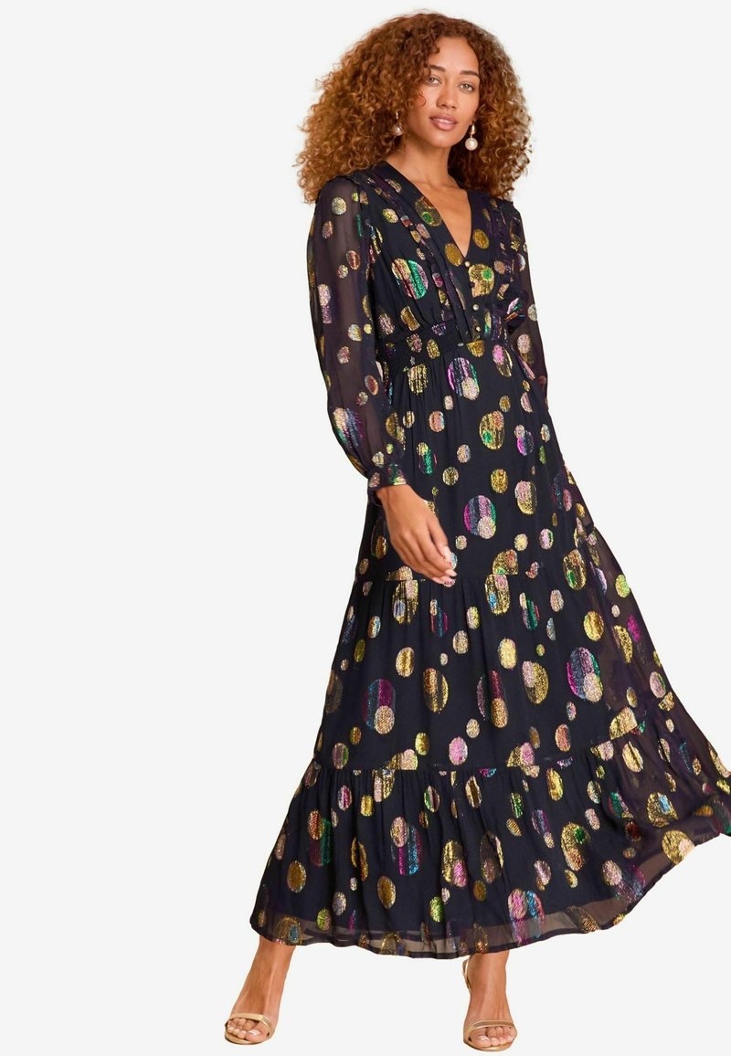 Rochie maxi din material transparent negru, cu motive circulare iridescente aurii și colorate. Are decolteu în V, mâneci lungi și un tiv în straturi.