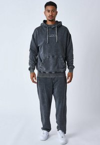 Hoodie gris, décoloré, avec une poche frontale et des cordons, associé à un pantalon fuselé assorti. Porté avec des baskets blanches.