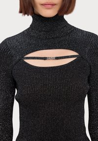 Top a collozzo nero a coste con un luccichio metallico, caratterizzato da un design con tagli e dettagli di cintura sul petto, che mette in evidenza un accento con logo.