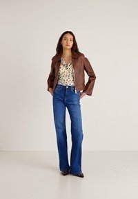 Barna bőr rövidített dzseki, mintás blúz, magas derekú, bővülő szárú kék farmernadrág, fekete szegecses hegyes orrú cipő. Sima textúrák, testhezálló kialakítás.