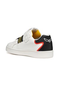 Witte leren sneaker met zwarte hiel, gele voering en zwart-geel gestreepte klittenbandsluiting. Heeft een rode accent op de hiel.