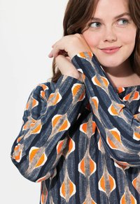 Maglietta a maniche lunghe di colore blu navy con un motivo astratto in arancione e beige. Il tessuto ha una finitura testurizzata e un design con vestibilità rilassata.