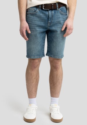 Heledad hallikad teksapüksid sirge lõikega, millel on esi-taskud, vöökohad ja veidi kulunud tekstuur. Kanda valgete sneakeritega.