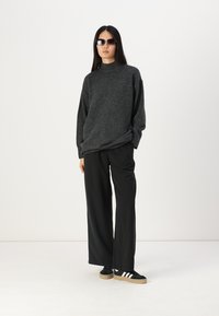 Grå oversized genser, svarte vide bukser, svarte solbriller og svarte joggesko med hvite striper. Glatt tekstur og avslappet passform.