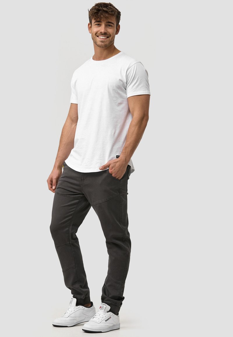 Camiseta blanca de manga corta combinada con pantalones oscuros de corte tapered y zapatillas blancas, con un ajuste casual y elementos de diseño mínimos.