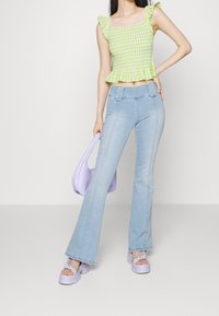 Zeleno-bílý kostkovaný peplum top s volánovými ramínky, spárovaný se světle modrými zvonovými džínami. Doplňky zahrnují levandulovou kabelku a odpovídající platformové boty.