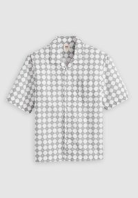 Camisa de manga corta en blanco con patrón geométrico de diamantes negros. Presenta un collar y un único bolsillo en el pecho. Fabricada con un tejido ligero.