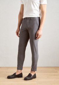 Gray tailored trousers with a slim fit, featuring a button closure, belt loops, and textured fabric. Paired with black leather loafers.